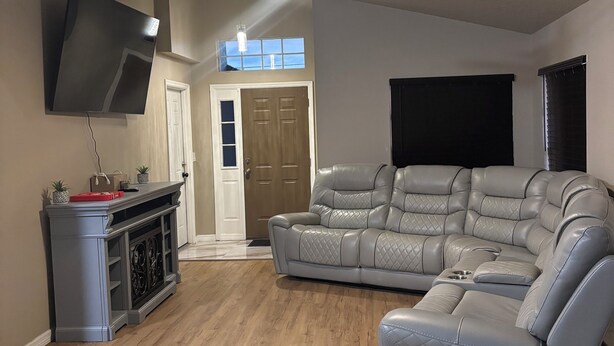 A spacious living room with a large sectional sofa, a flat-screen TV mounted on the wall, and a ceiling fan. - Orlando Getaway 3/2 Close to Theme Parks (Orlando)