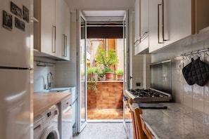 A compact kitchen with a built-in oven, a washing machine, and a small dining area. - Casa Luisa - WelcometoRhome (Roma)