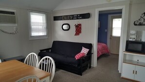 Een gezellige kamer met een zwarte bank, witte stoelen, een houten tafel en een televisie op een wit meubel.