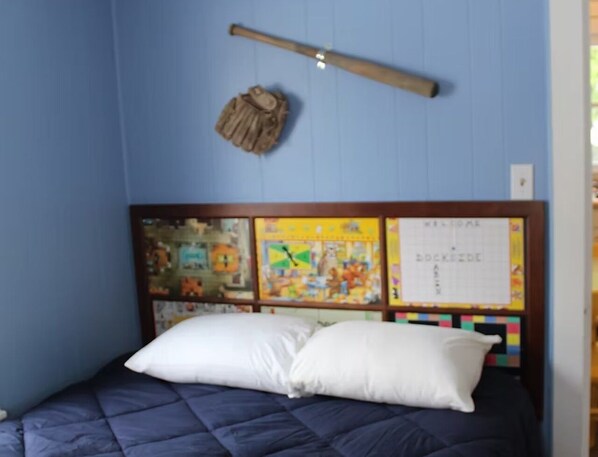 A bedroom with a bed, a headboard with a bulletin board, and a wooden stick on the wall.