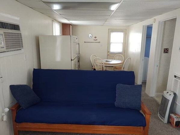 A compact living space with a blue sofa, a white refrigerator, a dining table with chairs, and a small heater.