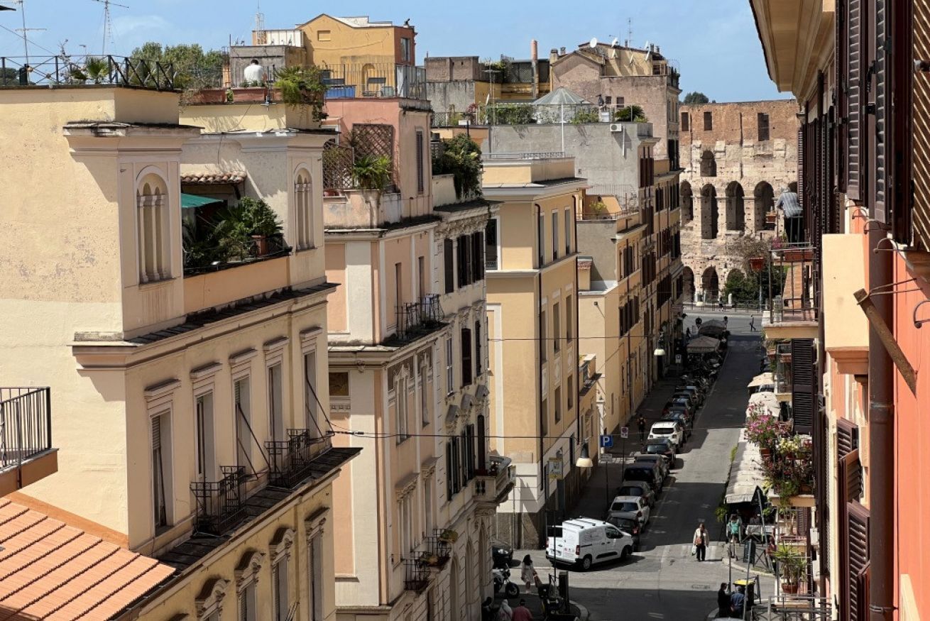 A narrow street lined with multi-story buildings, balconies, and a clear sky.