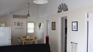 Ett rum med ett matbord, stolar, ett kylskåp, en takfläkt och en skylt på väggen med texten ”FÄRSKA ÄGG”.