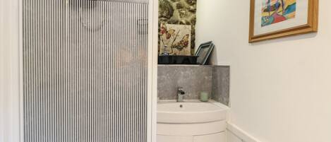 A bathroom with a shower, sink, and a framed painting on the wall.