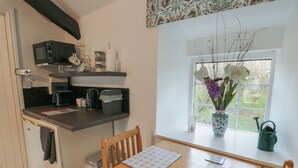 Een kleine keuken met een houten tafel, een raam met uitzicht op groen en een vaas met bloemen op de vensterbank.