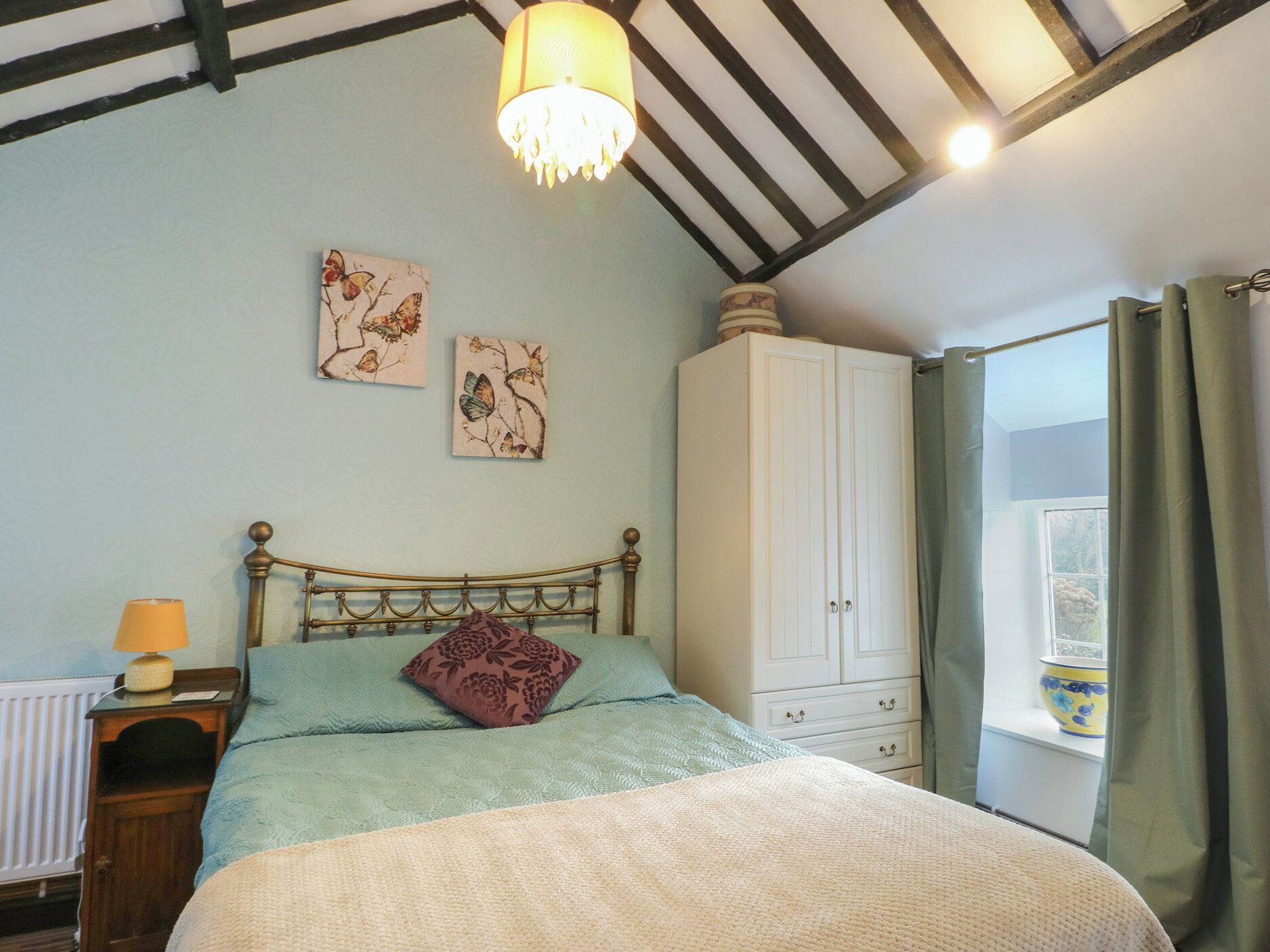 A bedroom with a bed, a nightstand, a wardrobe, and a window with curtains.