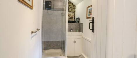 A narrow bathroom with a shower, a sink, and a small cabinet.