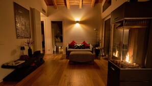 A cozy living room with a fireplace, wooden flooring, and a bed with red pillows. - Stella - panoramic attic in the BOTTONERA casa vacanza in alpine design (Chiavenna)