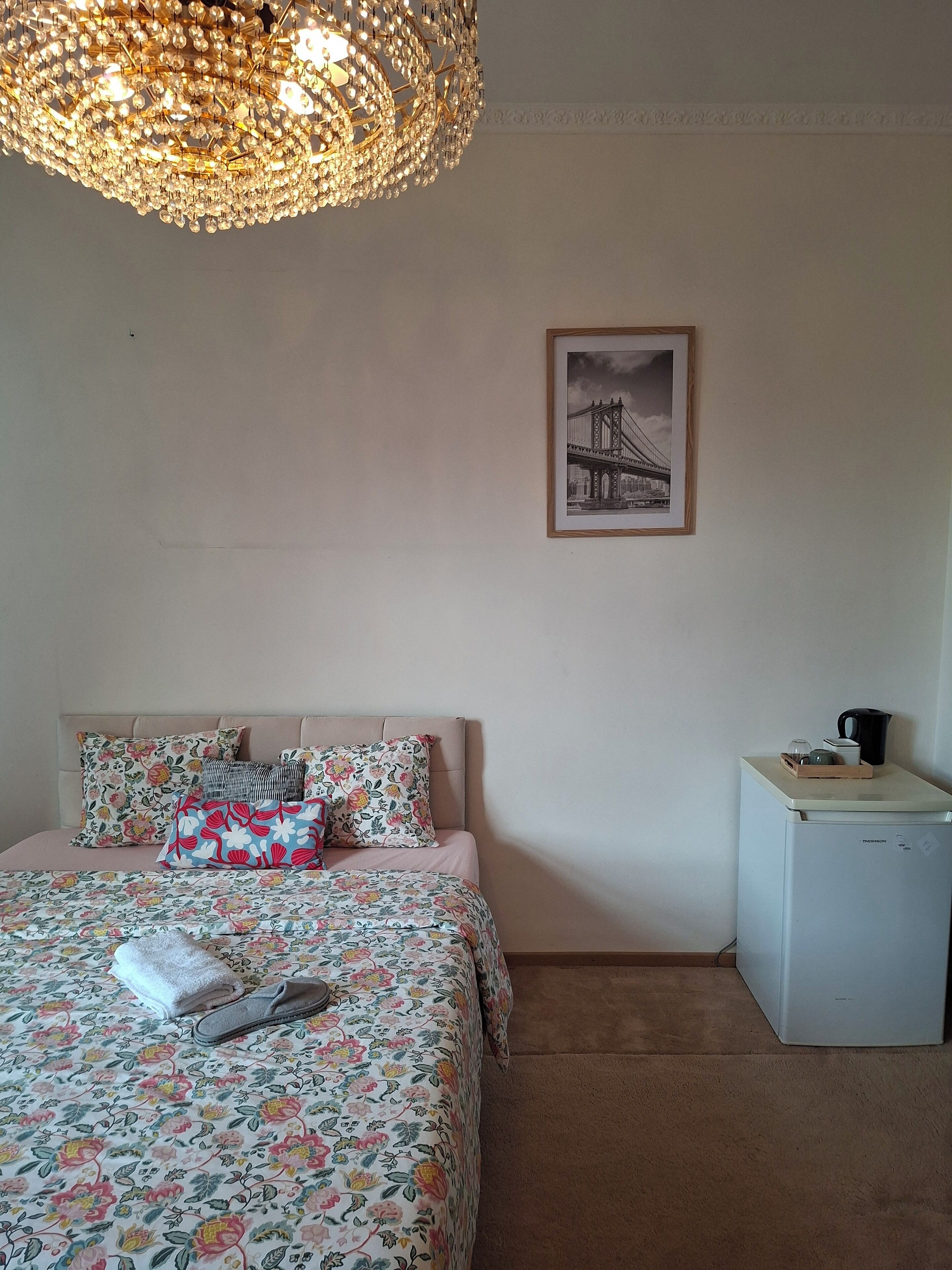 Une chambre à coucher avec un lit, des oreillers, un petit réfrigérateur et un tableau encadré accroché au mur.