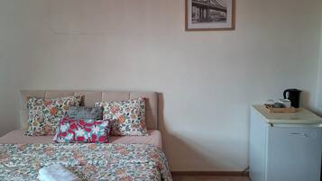 Une chambre à coucher avec un lit, des oreillers, un petit réfrigérateur et un tableau encadré accroché au mur.