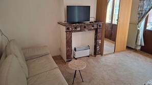 Una sala de estar con un sofá color beige, una mesita redonda, un televisor sobre un mueble de madera y un armario.