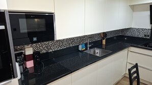 Una cocina moderna con encimera negra, armarios blancos, horno negro y salpicadero de azulejos.