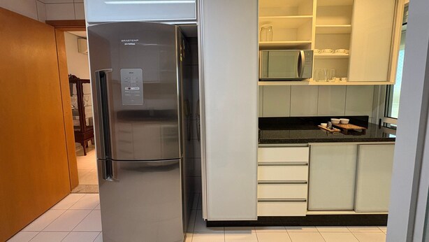 A kitchen with a stainless steel refrigerator, white cabinets, and a microwave. - Enjoy a Convenient Location and Comfort in Jardim Goias - Mfes (Goiânia)