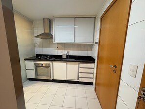 A compact kitchen with white cabinets, a black countertop, a stainless steel oven, and a wooden door. - Enjoy a Convenient Location and Comfort in Jardim Goias - Mfes (Goiânia)