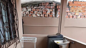 Pieni parveke, jossa on pyykinpesukone, pesuallas, pyykkiteline ja roskakori.