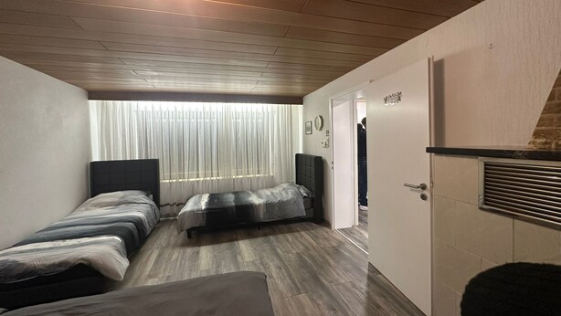 A modern bedroom with two beds, a wooden ceiling, a built-in wardrobe, and a window with sheer curtains. - Holiday Oasis 2.0 near Legoland Günzburg (Günzburg)