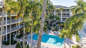 Un hotel a più piani con piscina centrale circondata da palme e lettini.