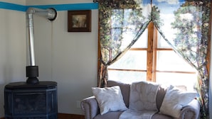 Un salon chaleureux avec un poêle à bois, un canapé et une fenêtre avec des rideaux.