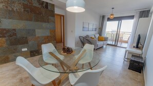 Un salón moderno con una mesa de comedor de cristal, sillas blancas y un sofá con cojines amarillos.