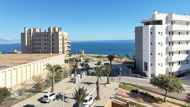 Un área urbana costera con edificios modernos, un cielo azul despejado y vista al mar.