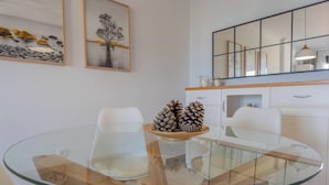Un comedor moderno con una mesa de vidrio, sillas blancas y un centro de mesa decorativo con piñas.