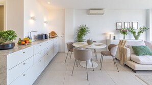 Una cocina moderna con armarios blancos, un comedor con una mesa y sillas redondas, y una sala de estar con un sofá y una mesa de centro.