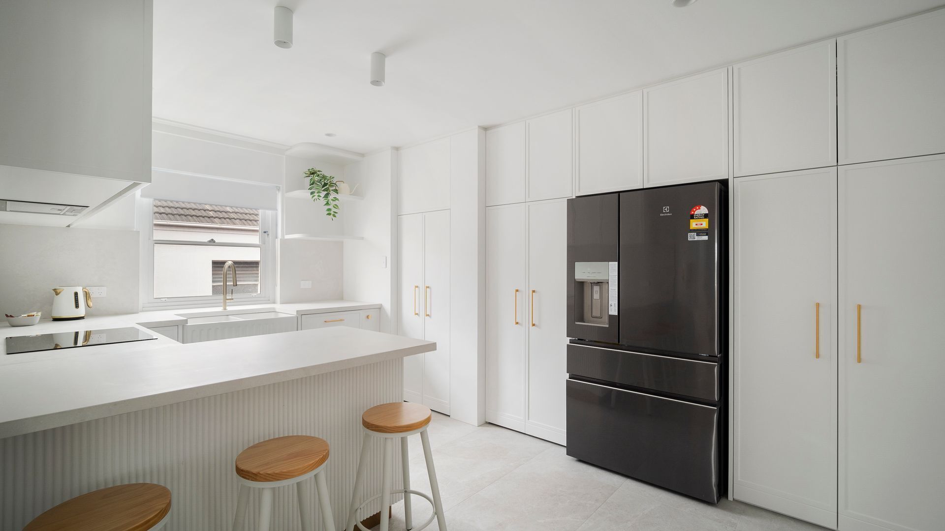 A modern kitchen with white cabinetry, a stainless steel refrigerator, and a white countertop.