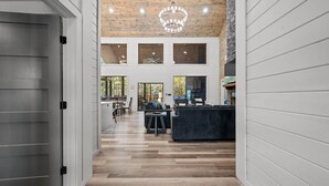 A spacious interior with a wooden ceiling, a dining area, and a kitchen with a dark-colored sofa. - NEW Pickleball Court Luxury Modern 6BR Cabin, Hot Tub, Game Room, Playset (Broken Bow)