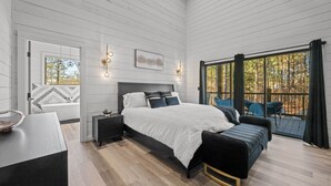 A bedroom with a bed, bedside tables, a bench, and a view of the outdoors. - NEW Pickleball Court Luxury Modern 6BR Cabin, Hot Tub, Game Room, Playset (Broken Bow)