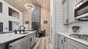 A modern kitchen with a central island, built-in appliances, and a stone accent wall. - NEW Pickleball Court Luxury Modern 6BR Cabin, Hot Tub, Game Room, Playset (Broken Bow)
