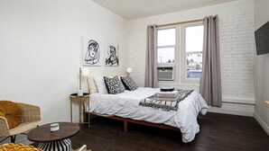 Un dormitorio con cama, una silla, una mesita y una obra de arte en la pared.