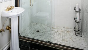 Un baño moderno con ducha envuelta en vidrio, lavamanos pedestal y espejo de tocador.