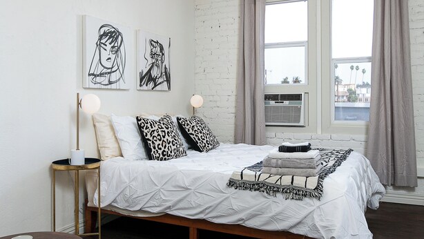 Un dormitorio moderno con cama, mesita de noche, silla y una obra de arte en la pared.