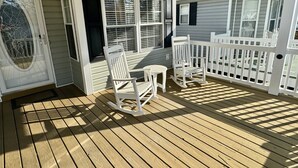 Una terraza de madera con mecedoras y una valla blanca.