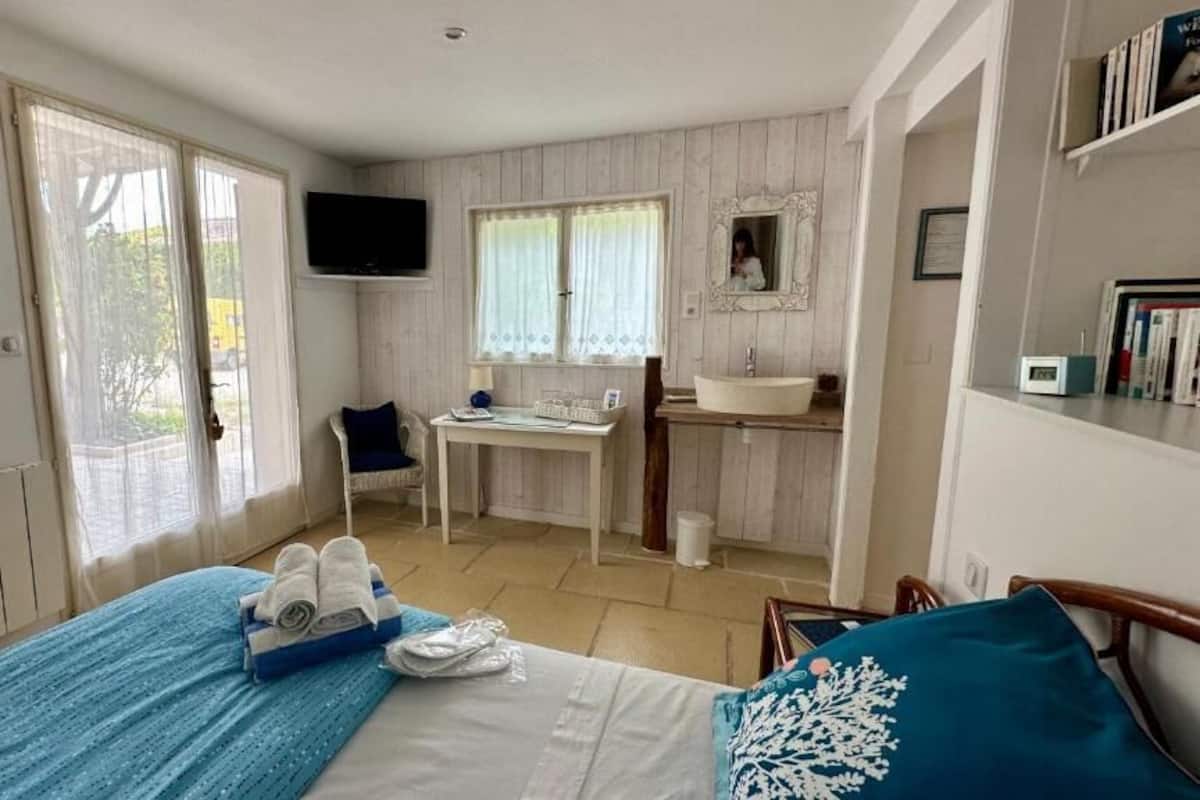 A bedroom with a bed, a desk, a chair, a sink, and a television.