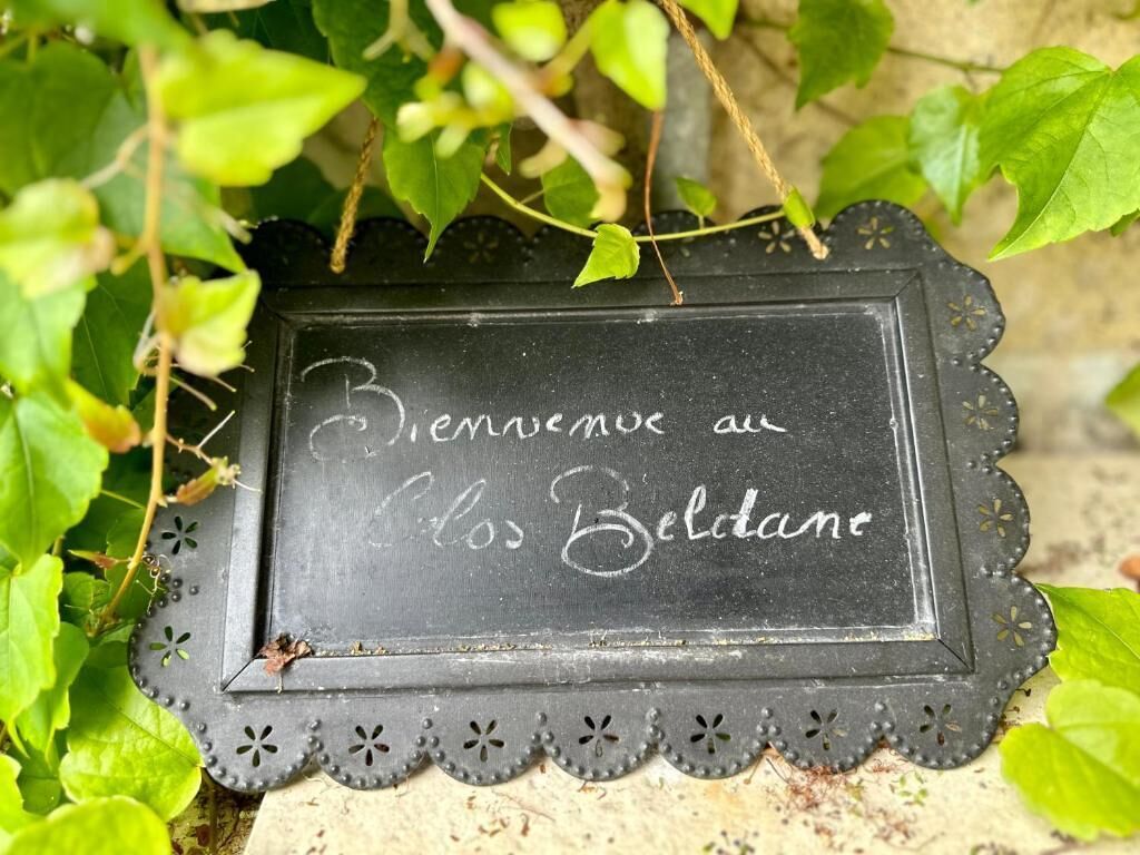 A black sign with white text that reads "Bienvenue au Les Belidane" surrounded by green foliage.