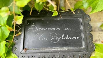 A black sign with white text that reads "Bienvenue au Les Belidane" surrounded by green foliage.