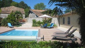 A swimming pool with lounge chairs, a stone building, and a tiled-roof house in the background. - Clos Beldane (Le Tâtre)