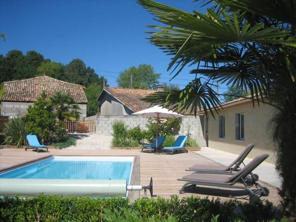 A swimming pool with lounge chairs, a stone building, and a tiled-roof house in the background. - Clos Beldane (Le Tâtre)