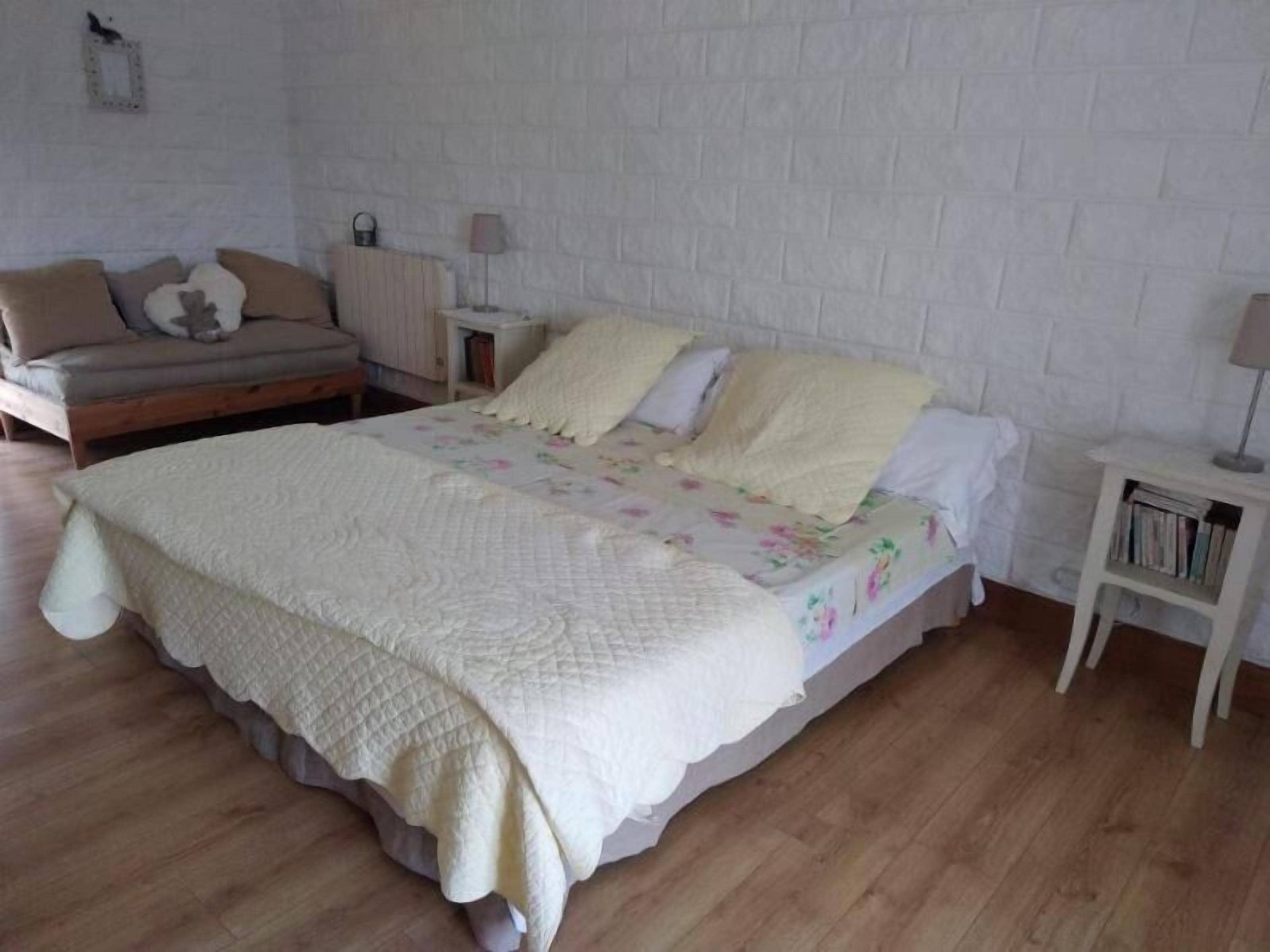 A bedroom with a bed, a nightstand, a lamp, a bookshelf, and a sofa.