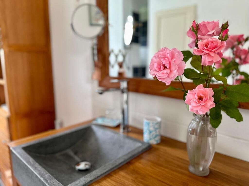 A bathroom with a wooden vanity, a mirror, and a vase with pink flowers.
