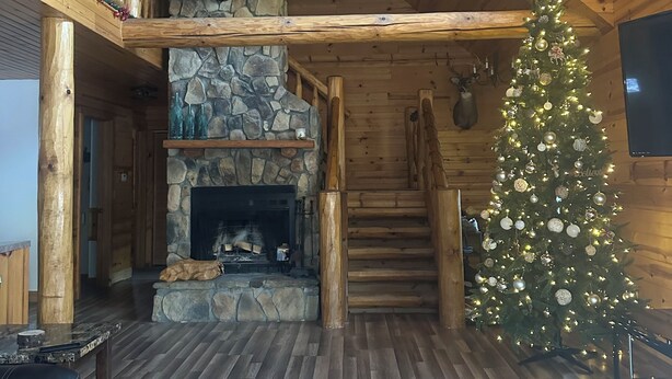 A log cabin interior with a stone fireplace, wooden beams, a Christmas tree, and a staircase. - Mountain feel/10 minutes from the city! (Pittsburgh)