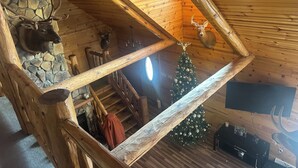 A rustic cabin interior with a stone wall, wooden staircase, a decorated Christmas tree, and mounted animal heads. - Mountain feel/10 minutes from the city! (Pittsburgh)