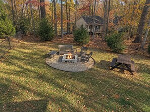 A circular outdoor seating area with a fire pit, surrounded by a grassy lawn and trees.