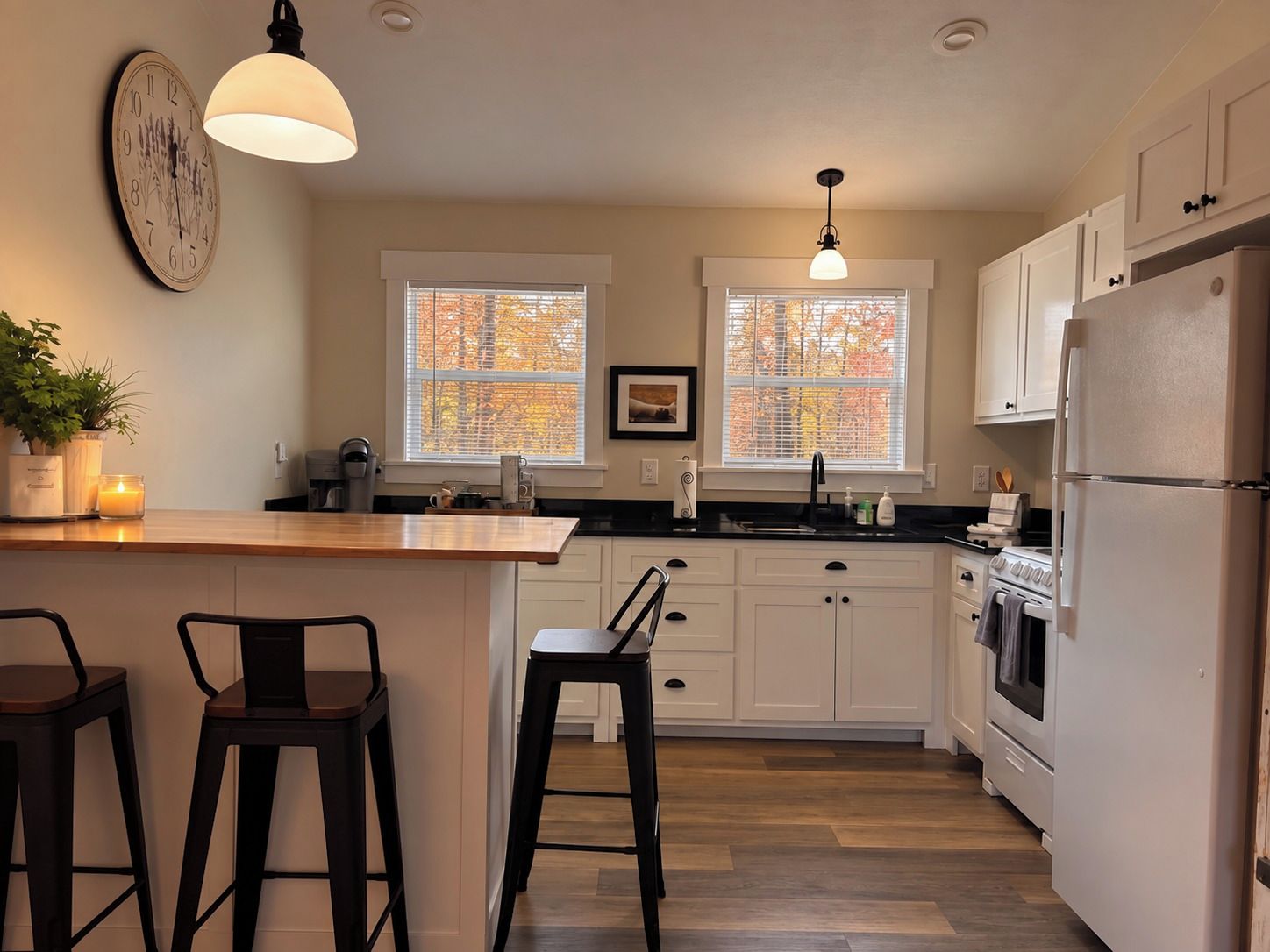 Une cuisine avec un îlot central en bois, des meubles blancs, un réfrigérateur et une horloge au mur.