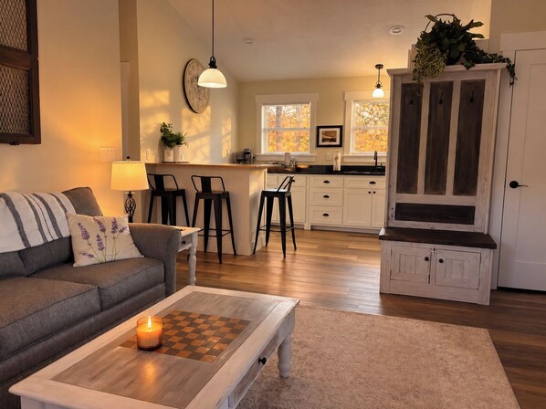 A living room with a sofa, a coffee table with a candle, and a kitchen in the background.