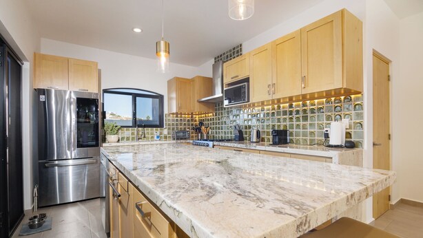 A modern kitchen with stainless steel appliances, wooden cabinets, and a marble countertop. - Luxury Home in Brand New Complex in Cerritos Beach (El Pescadero)