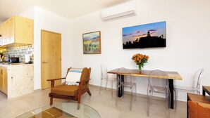 A dining area with a wooden table, clear chairs, a glass coffee table, and a painting of a sunset. - Luxury Home in Brand New Complex in Cerritos Beach (El Pescadero)
