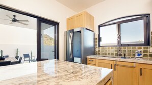A modern kitchen with a marble countertop, stainless steel appliances, wooden cabinets, and a view through a sliding door. - Luxury Home in Brand New Complex in Cerritos Beach (El Pescadero)