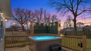 Ein Whirlpool auf einer Holzterrasse mit Blick auf ein Haus und Bäume.